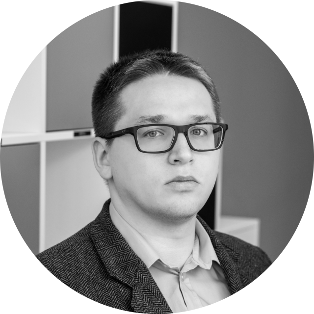 Czarno-biały portret osoby w okularach i marynarce, patrzącej w kamerę, z geometrycznym wzorem tła.